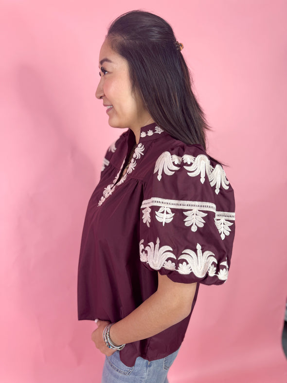 Side view of embroidered puff sleeves on burgundy top 